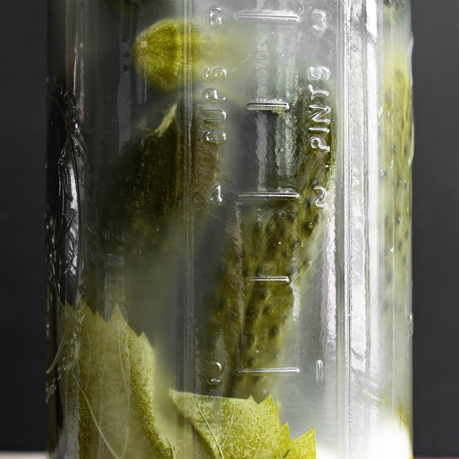 Closeup of finished, fully fermented half-sour pickles, immersed in cloudy brine in a half-gallon jar.