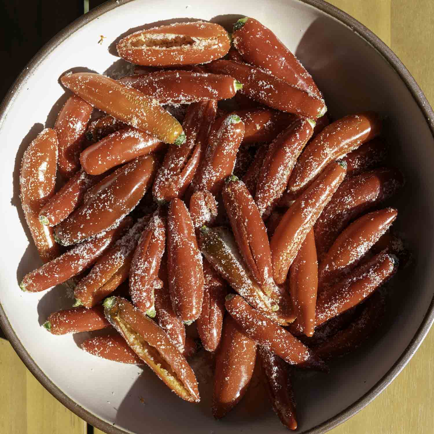 Closeup of a bowl of seeded and salted red serrano peppers.