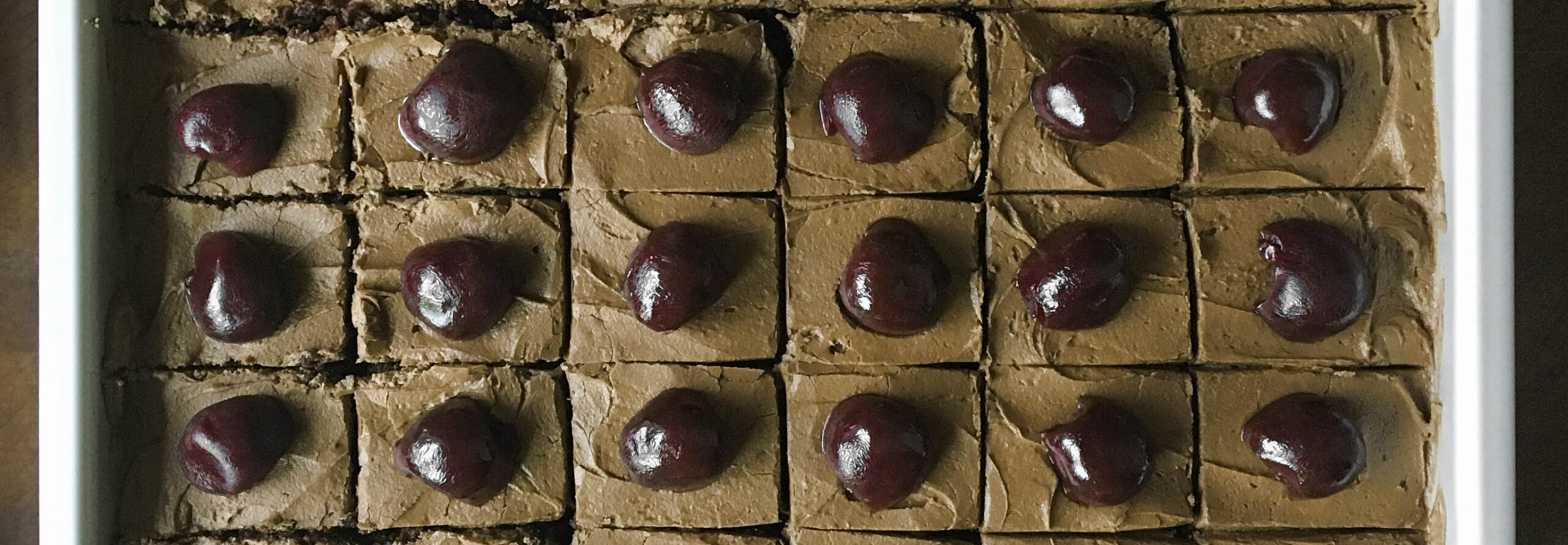 Overhead closeup of a Texas sheet cake, cut into square slices. Each slice has been topped with one plump bourbon-soaked cherry.