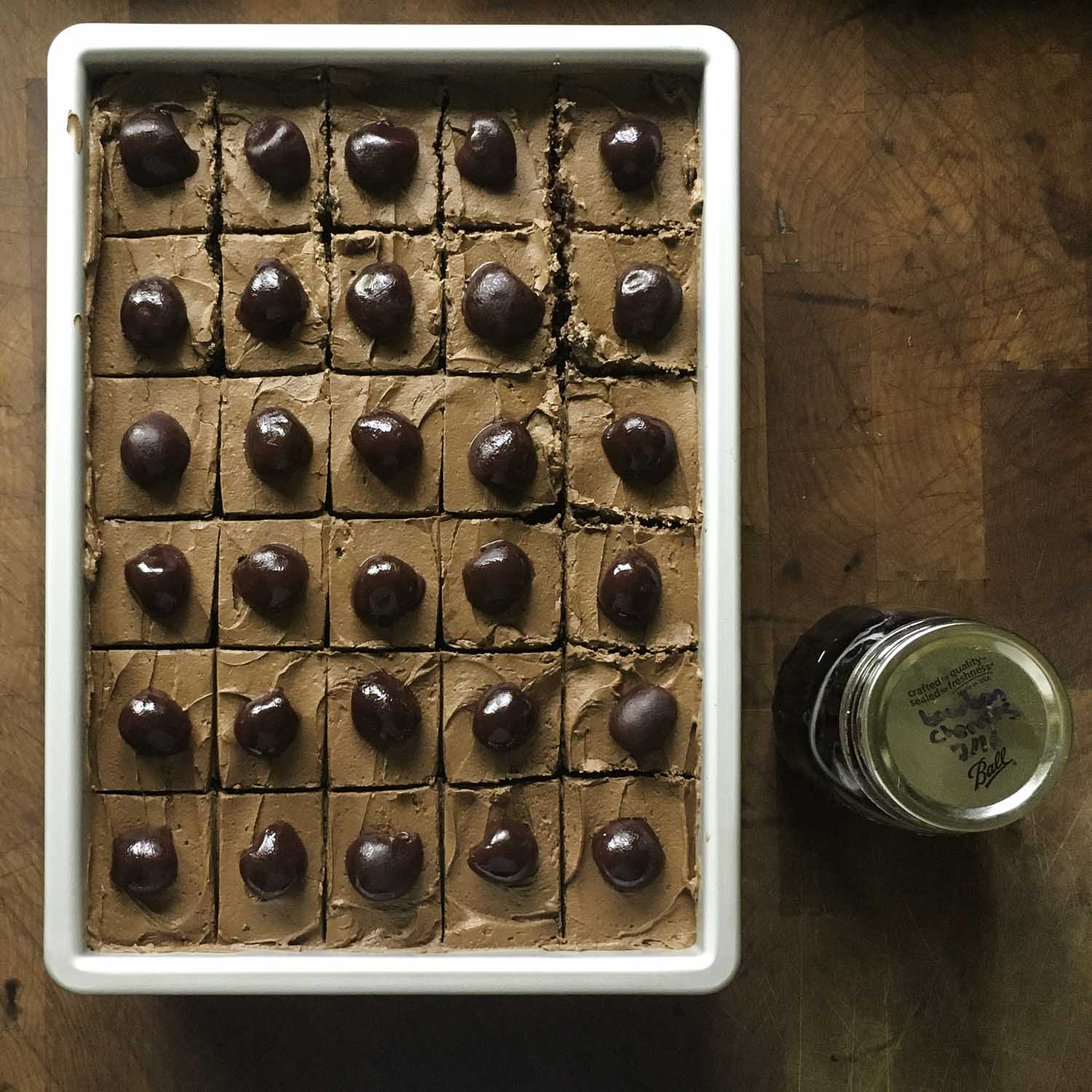 Overhead view of a Texas sheet cake, cut into square slices. Each slice has been topped with one plump bourbon-soaked cherry.
