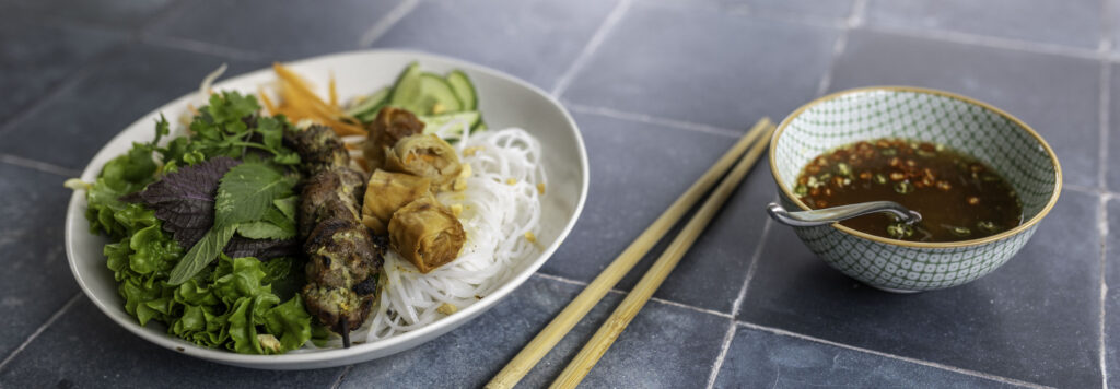 Bún thit nuong, served with a small bowl of nuoc cham on a worn black tile surface.