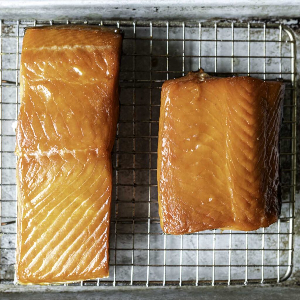 Closeup of two portions of hot-smoked salmon, resting on a cooling rack set over a quarter sheet pan.
