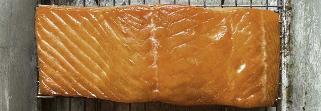 Closeup of a portion of hot-smoked salmon placed on a cooling rack set over a quarter sheet pan.