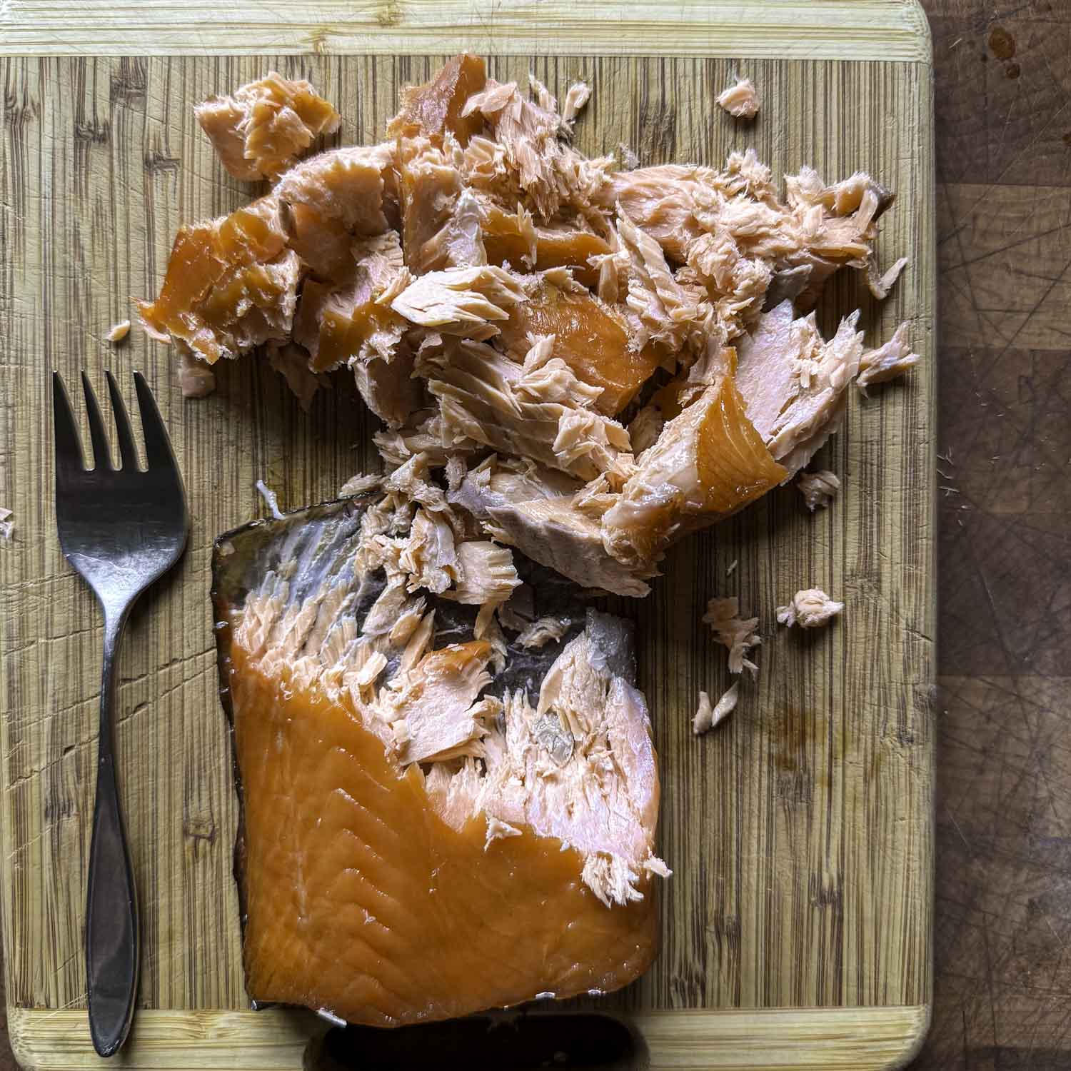 Overhead view of a portion of hot-smoked salmon partially flaked on a cutting board with a fork.