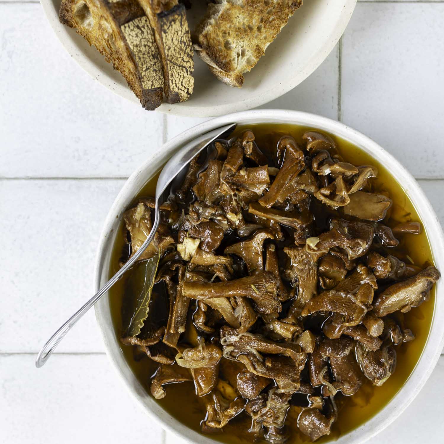 Overhead view of mushroom confit, served in a bowl with slices of toasted sourdough.