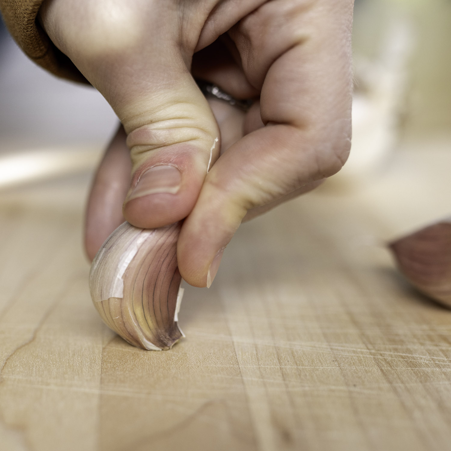 Closeup of the author holding a garlic clove upright on a cutting board and applying pressure.