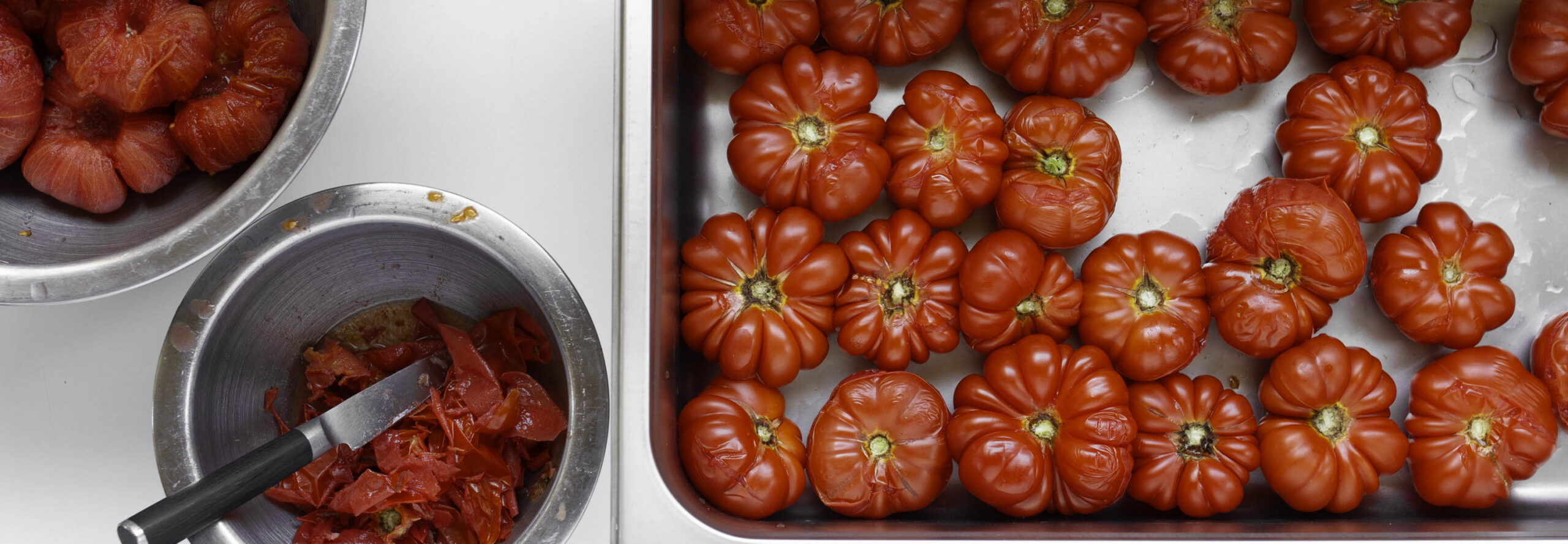 Overhead view of a workspace where blanched tomatoes are being peeled one by one.