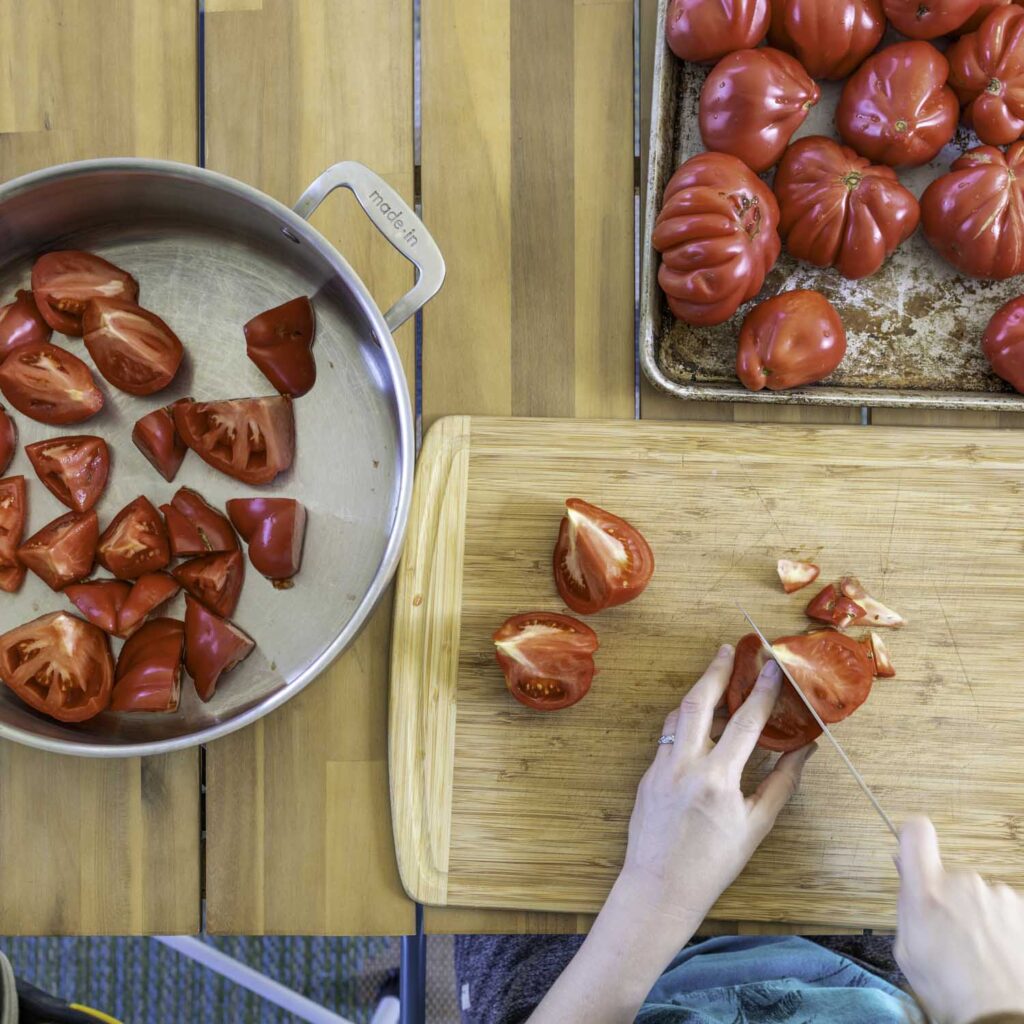 Overhead view of Astiana tomatoes being quartered, cored, and collected in a large rondeau pan.