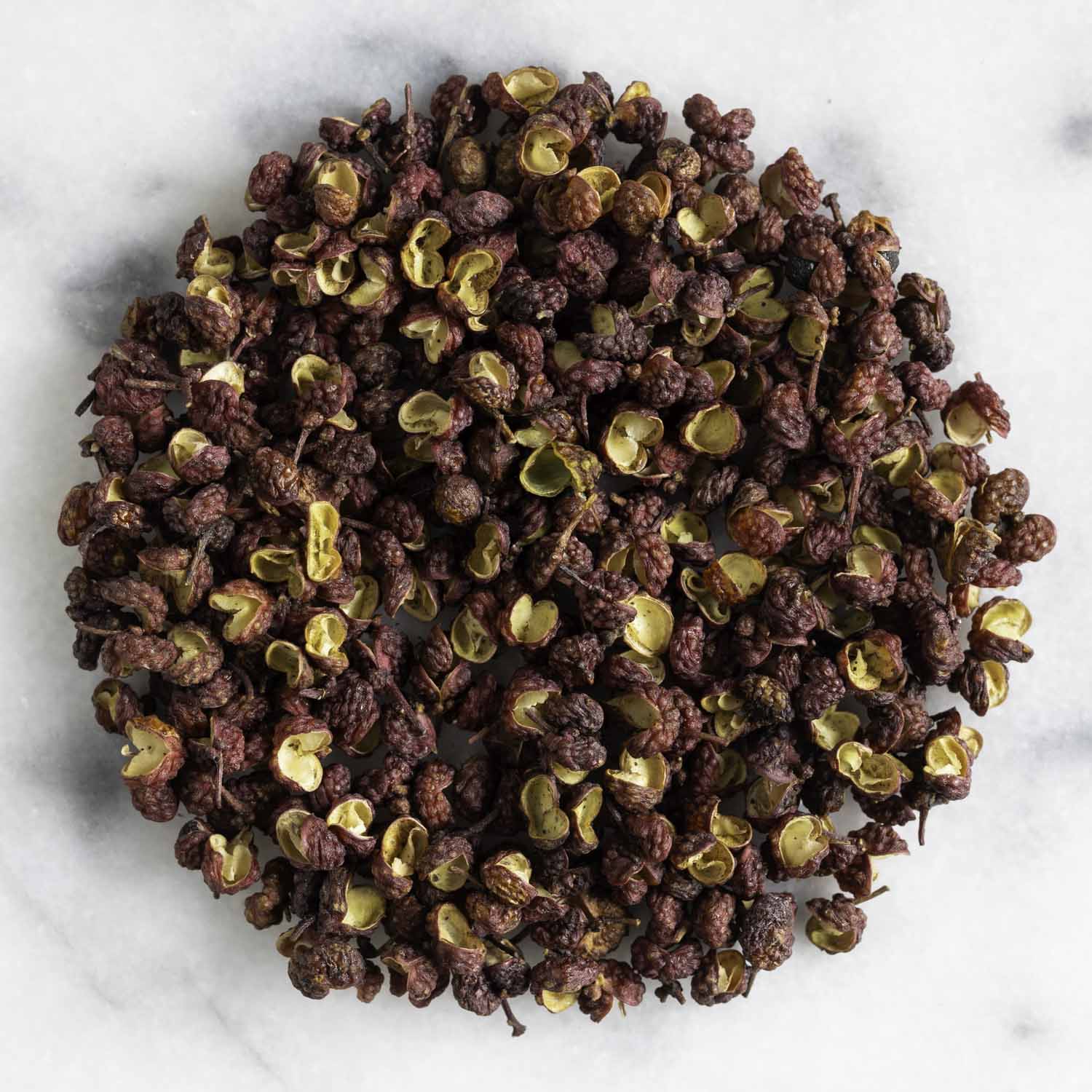 Closeup of a circular pile of dried red Sichuan pepper on a white marble surface.
