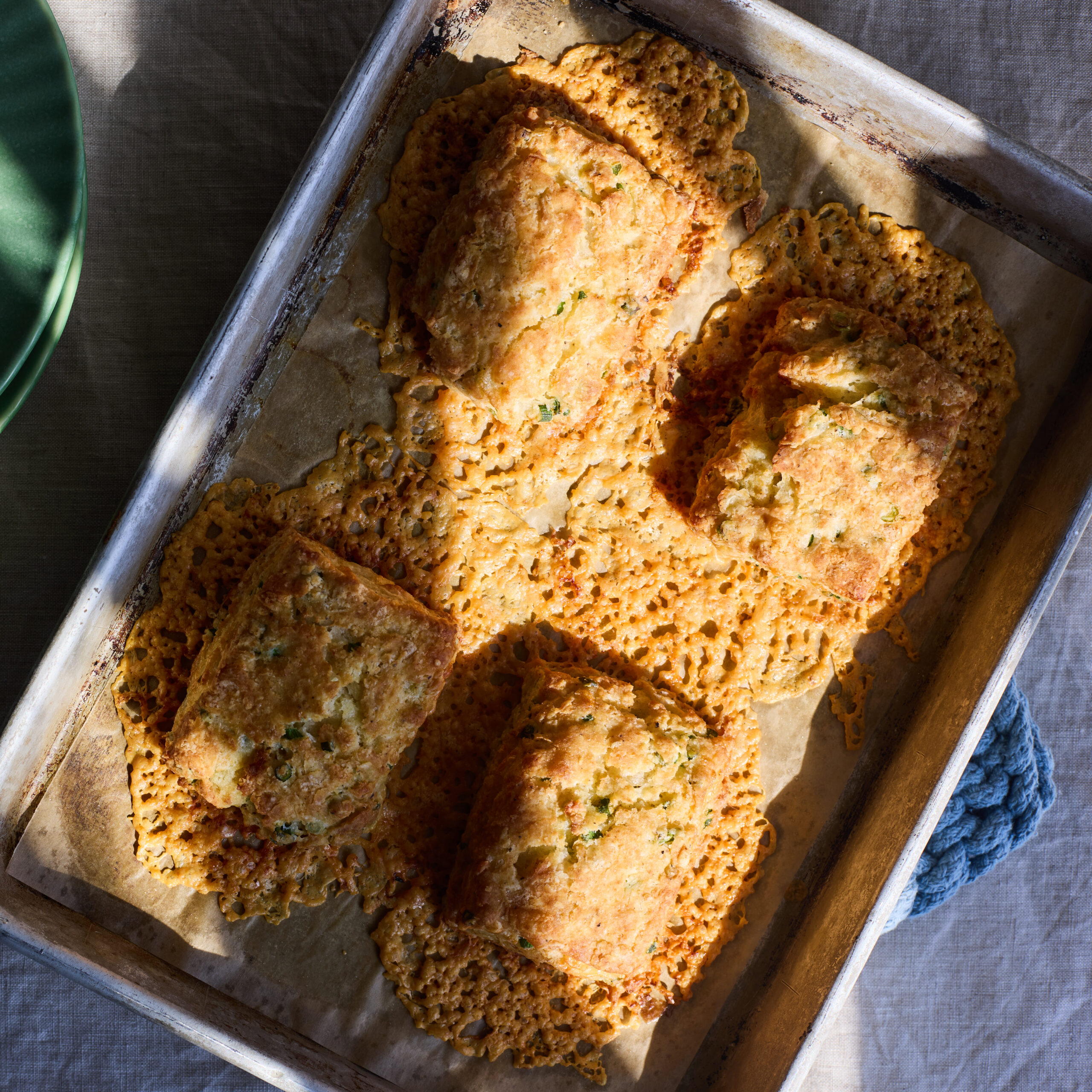Moody overhead shot of Megan's cheddar-scallion biscuits on a parchment-lined sheet pan, fresh from the oven.